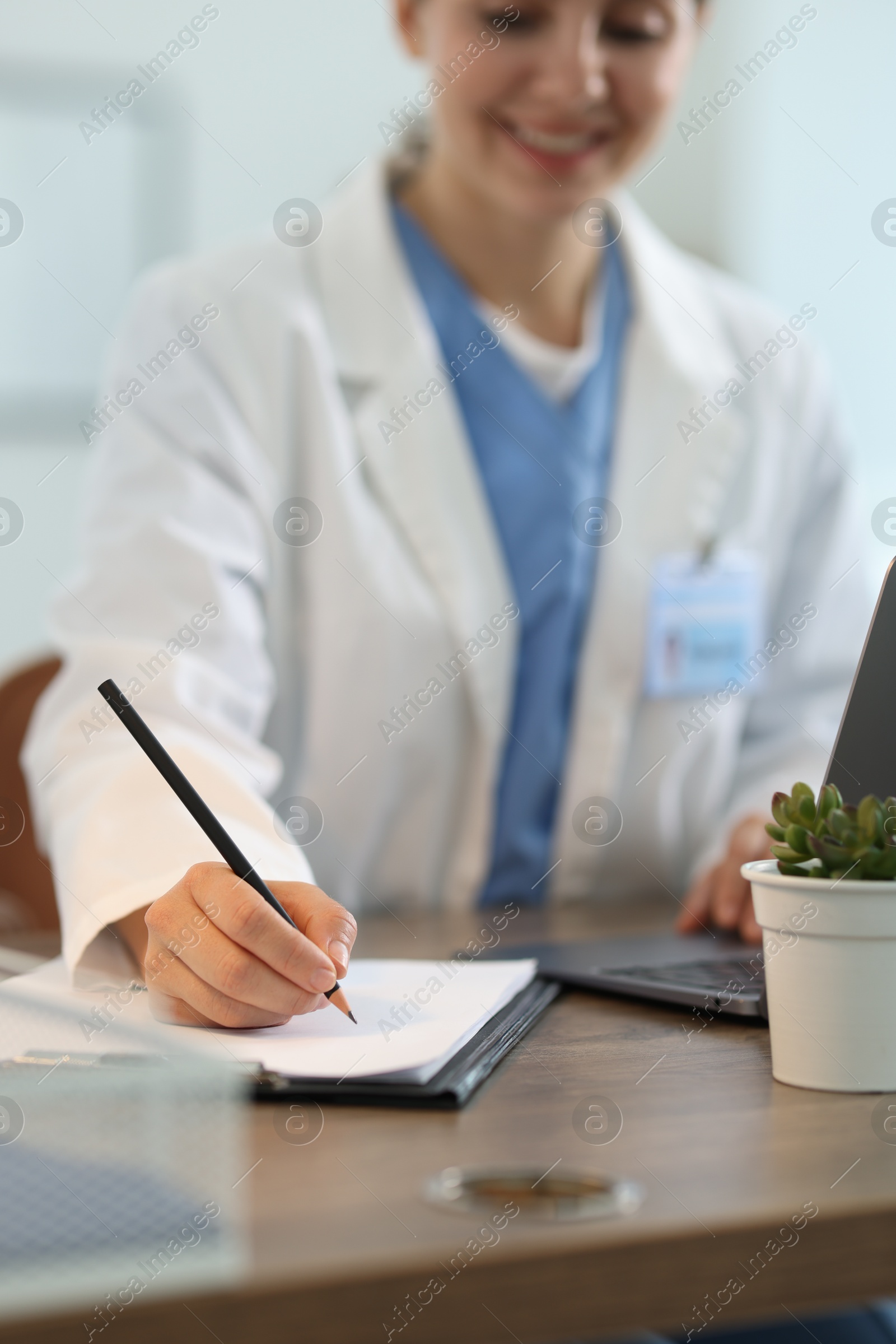 Photo of Telemedicine. Doctor making notes while having video call with patient via laptop indoors, closeup