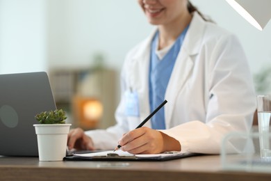 Photo of Telemedicine. Doctor making notes while having video call with patient via laptop indoors, closeup