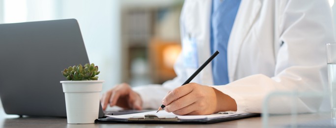 Photo of Telemedicine. Doctor making notes while having video call with patient via laptop indoors, closeup