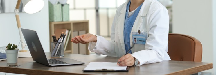 Photo of Telemedicine. Doctor making notes while having video call with patient via laptop indoors, closeup