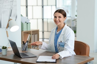 Photo of Telemedicine. Doctor making notes while having video call with patient via laptop indoors