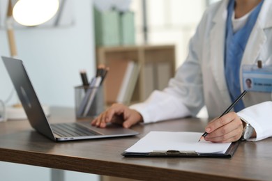 Photo of Telemedicine. Doctor making notes while having video call with patient via laptop indoors, closeup