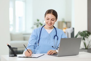 Photo of Telemedicine. Doctor making notes while having video call with patient via laptop indoors