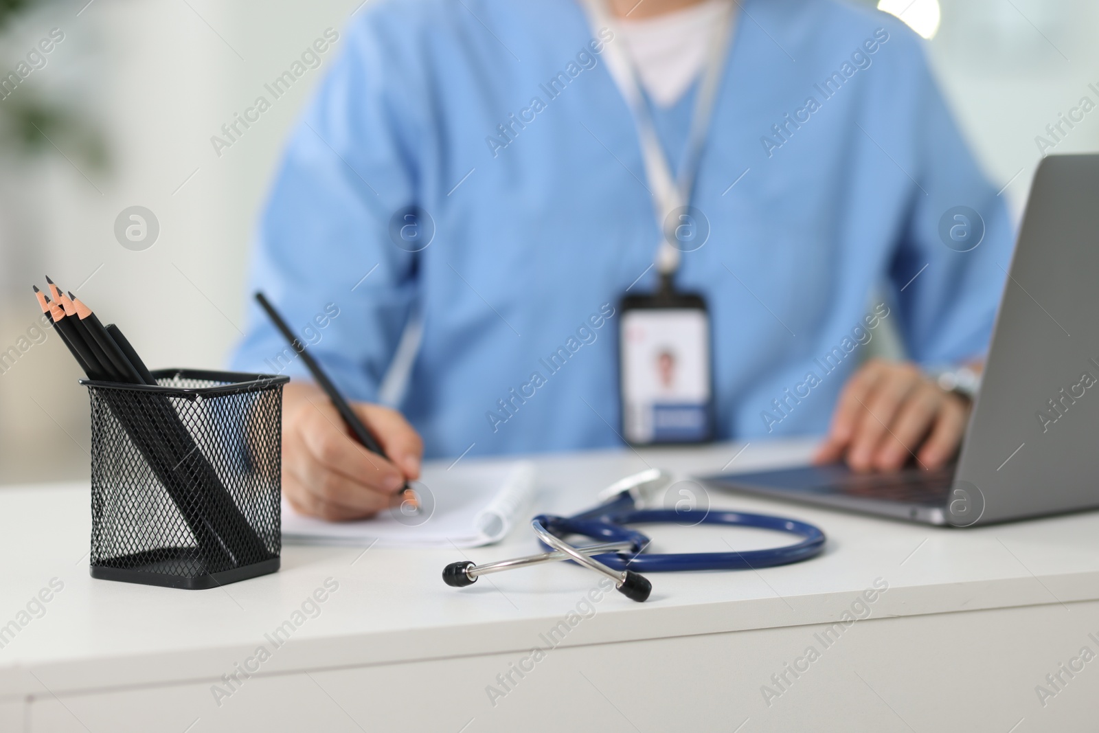 Photo of Telemedicine. Doctor making notes while having video call with patient via laptop indoors, closeup