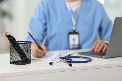Photo of Telemedicine. Doctor making notes while having video call with patient via laptop indoors, closeup