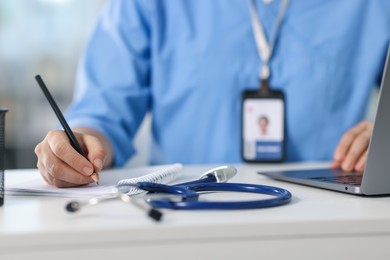 Photo of Telemedicine. Doctor making notes while having video call with patient via laptop indoors, closeup