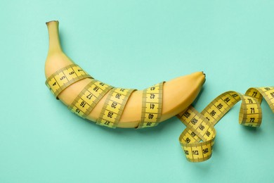 Photo of Sex education. Banana with measuring tape on turquoise background, top view