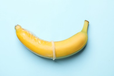 Photo of Sex education. Banana with condom on light blue background, top view