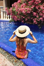 Photo of Girl in straw hat at poolside outdoors on sunny day, back view