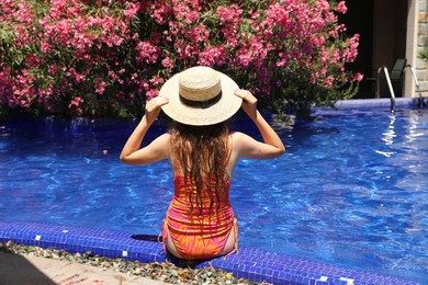 Photo of Girl in straw hat at poolside outdoors on sunny day, back view
