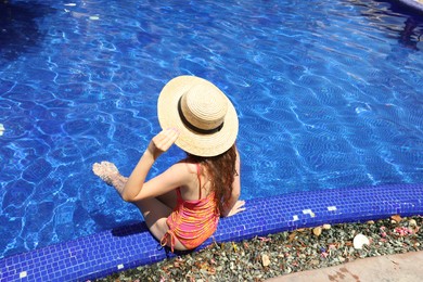 Photo of Girl in straw hat at poolside outdoors on sunny day, back view