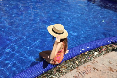 Photo of Girl in straw hat at poolside outdoors on sunny day, back view