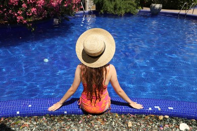 Photo of Girl in straw hat at poolside outdoors on sunny day, back view