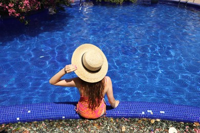 Photo of Girl in straw hat at poolside outdoors on sunny day, back view