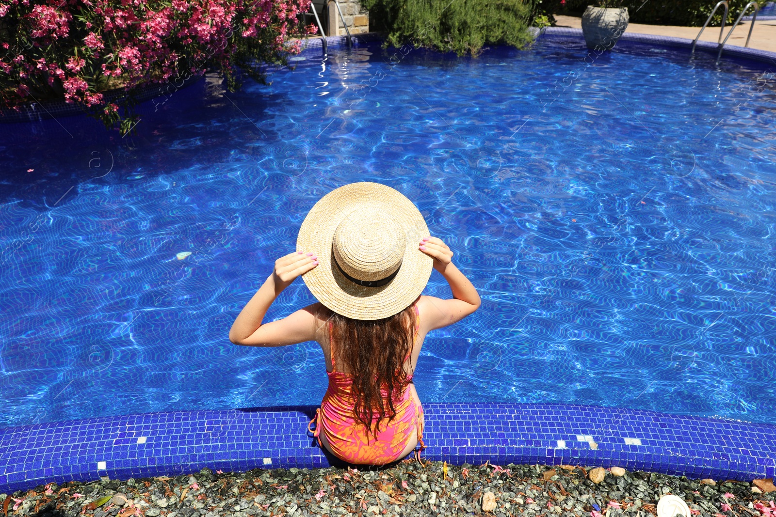 Girl in straw hat at poolside outdoors on sunny day, back view Photo of Girl in straw hat at poolside outdoors on sunny day, back view