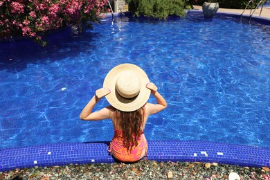 Photo of Girl in straw hat at poolside outdoors on sunny day, back view