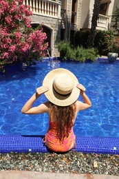 Photo of Girl in straw hat at poolside outdoors on sunny day, back view