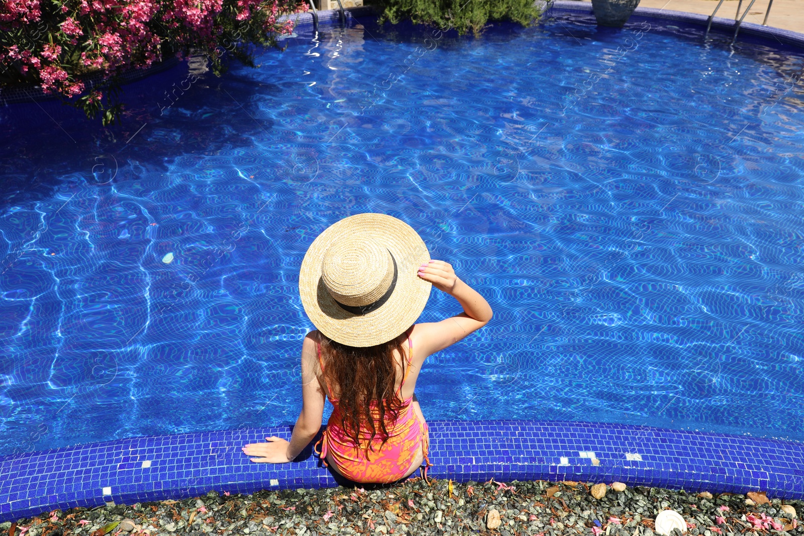 Girl in straw hat at poolside outdoors on sunny day, back view Photo of Girl in straw hat at poolside outdoors on sunny day, back view