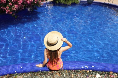 Photo of Girl in straw hat at poolside outdoors on sunny day, back view