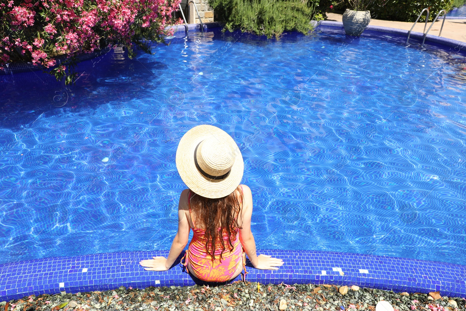 Girl in straw hat at poolside outdoors on sunny day, back view Photo of Girl in straw hat at poolside outdoors on sunny day, back view