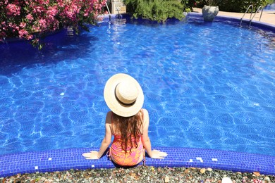 Photo of Girl in straw hat at poolside outdoors on sunny day, back view