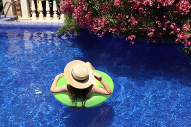 Photo of Girl on inflatable ring in swimming pool outdoors on sunny day, back view