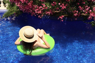 Photo of Girl on inflatable ring in swimming pool outdoors on sunny day, back view. Space for text