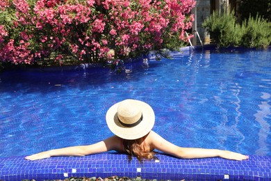 Photo of Girl with straw hat in swimming pool outdoors on sunny day, back view