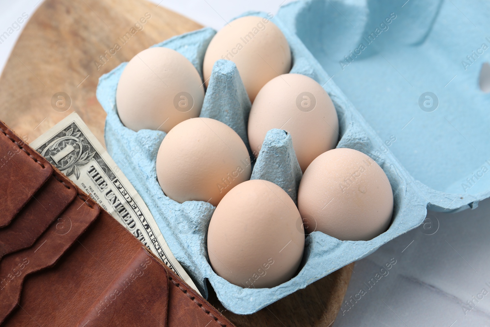 Photo of Raw chicken eggs in egg carton and wallet with dollar banknote on white tiled table, closeup