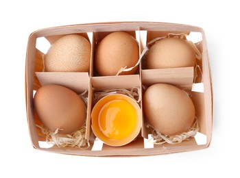 Photo of Whole and broken chicken eggs in wooden tray isolated on white, top view