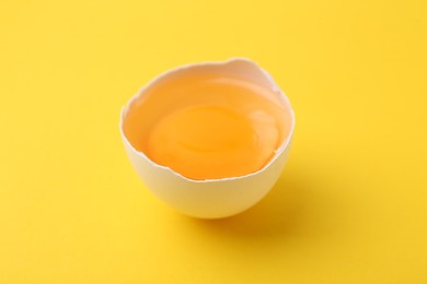 Photo of One broken chicken egg on yellow background, closeup