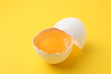 Photo of One broken chicken egg on yellow background, closeup