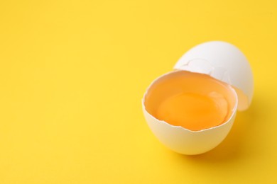 Photo of One broken chicken egg on yellow background, closeup. Space for text