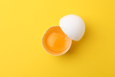 Photo of One broken chicken egg on yellow background, top view