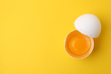 Photo of One broken chicken egg on yellow background, top view. Space for text