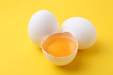 Photo of Whole and broken chicken eggs on yellow background, closeup