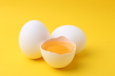 Photo of Whole and broken chicken eggs on yellow background, closeup