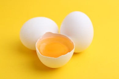 Photo of Whole and broken chicken eggs on yellow background, closeup