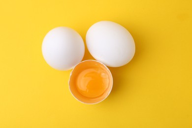 Photo of Whole and broken chicken eggs on yellow background, top view