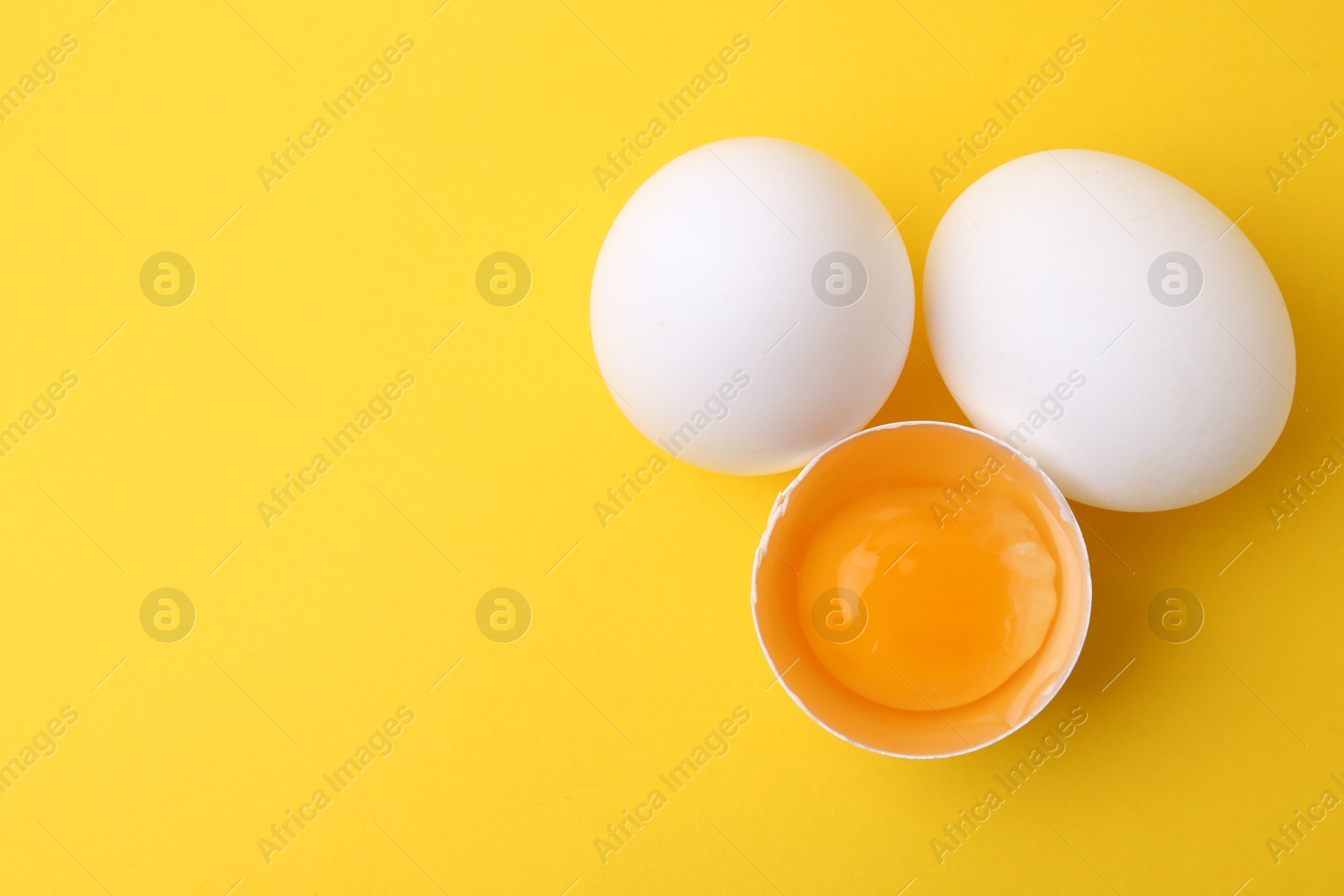 Whole and broken chicken eggs on yellow background, top view. Space for text Photo of Whole and broken chicken eggs on yellow background, top view. Space for text