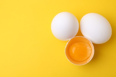 Photo of Whole and broken chicken eggs on yellow background, top view. Space for text