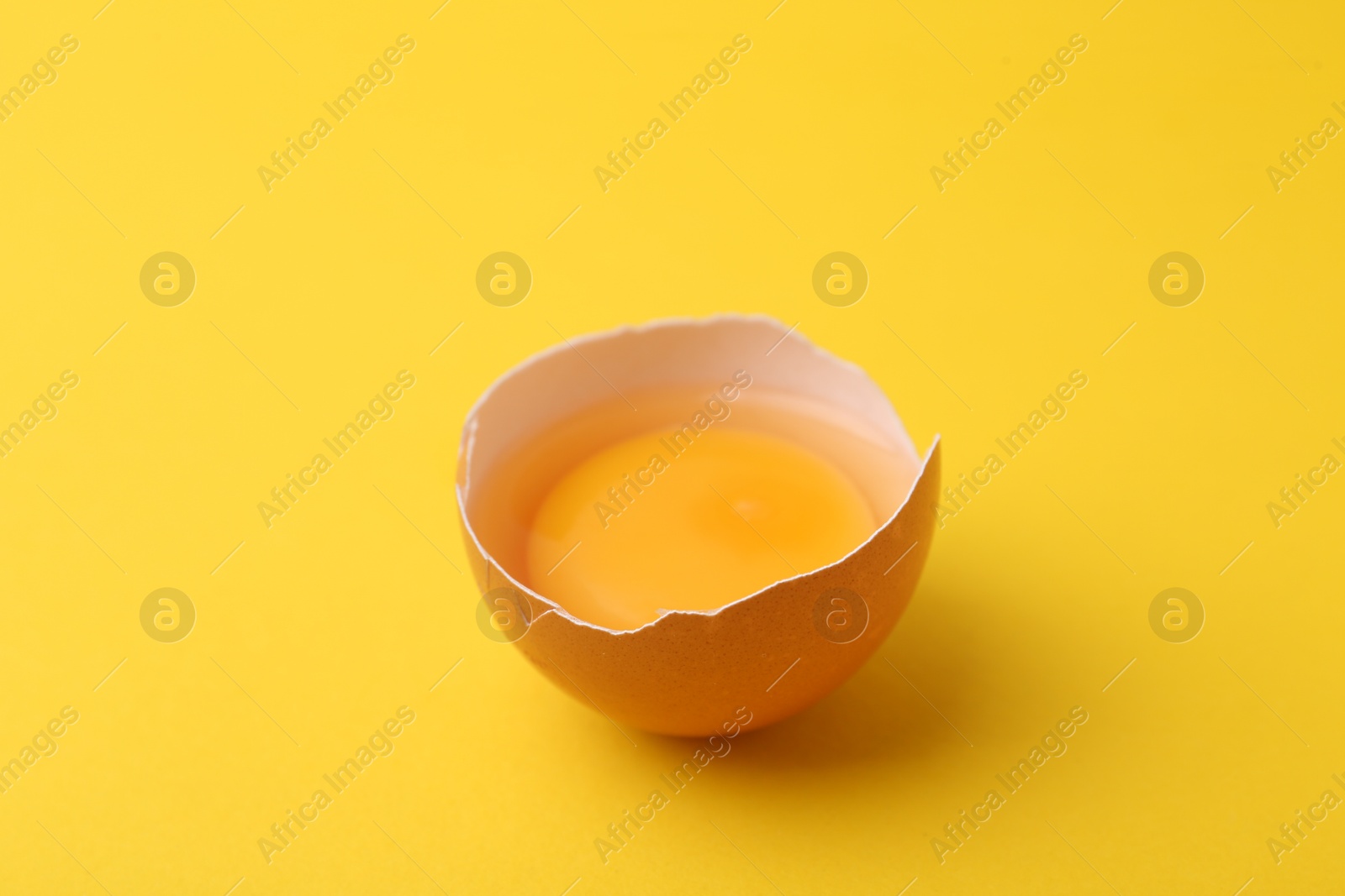 One broken chicken egg on yellow background, closeup Photo of One broken chicken egg on yellow background, closeup