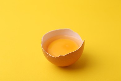 Photo of One broken chicken egg on yellow background, closeup