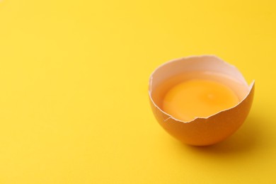 Photo of One broken chicken egg on yellow background, closeup. Space for text
