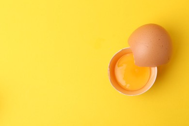 Photo of One broken chicken egg on yellow background, top view. Space for text