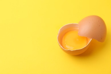 Photo of One broken chicken egg on yellow background, closeup. Space for text