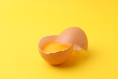 Photo of One broken chicken egg on yellow background, closeup