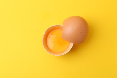 Photo of One broken chicken egg on yellow background, top view