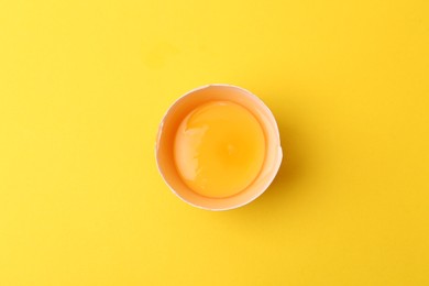 Photo of One broken chicken egg on yellow background, top view