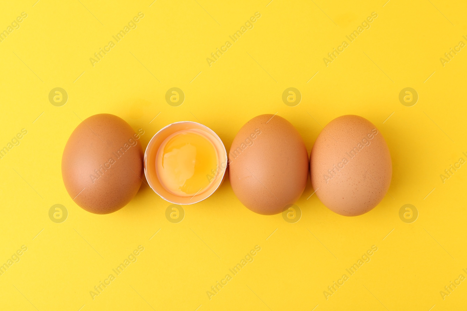 Whole and broken chicken eggs on yellow background, top view Photo of Whole and broken chicken eggs on yellow background, top view